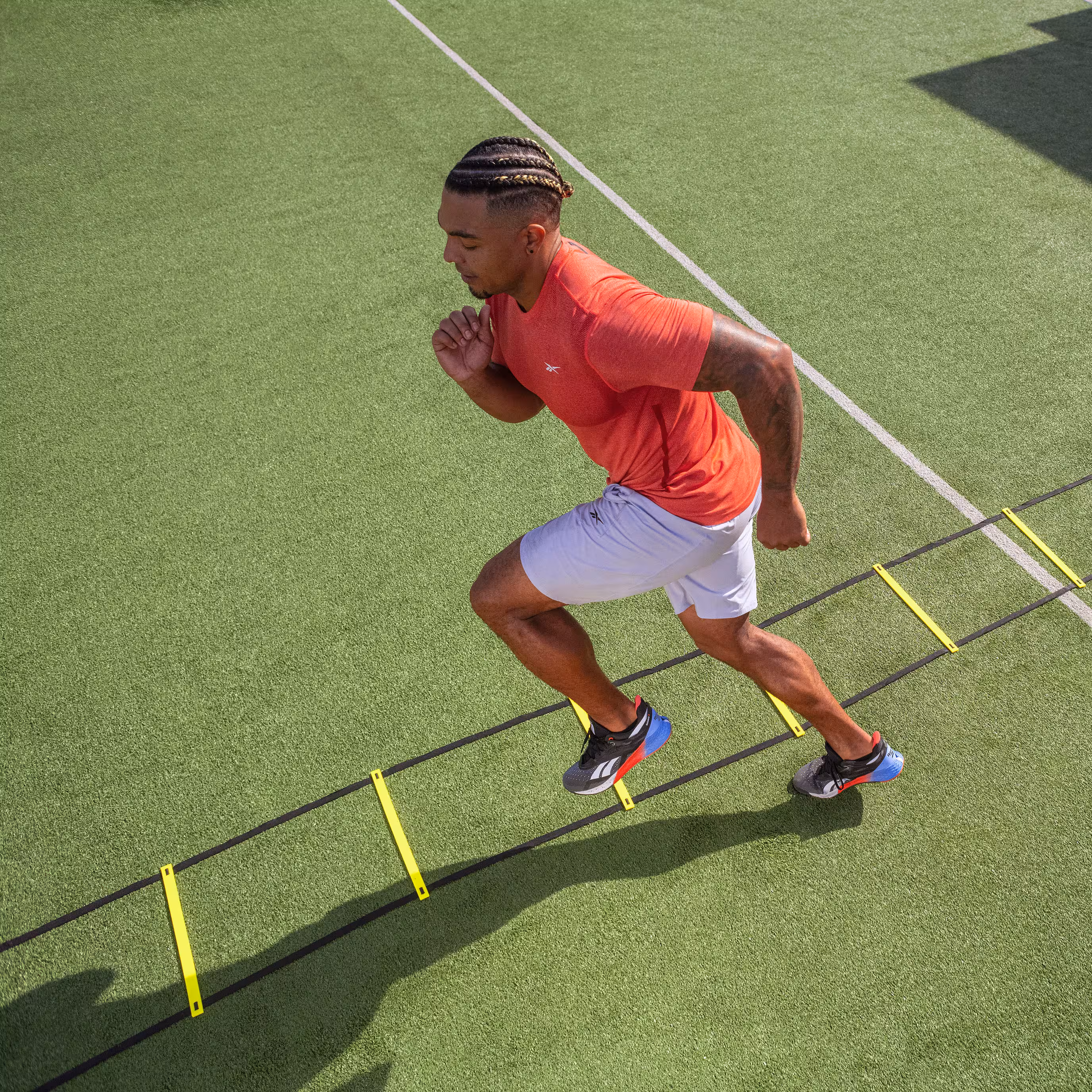 Male athlete sprinting through an agility ladder drill wearing Reebok Nano X training shoes.