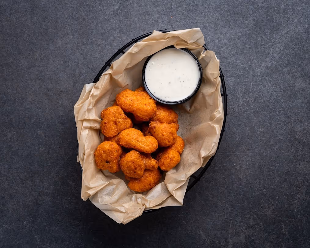 A bowl of corn dogs with a container of dipping sauce.