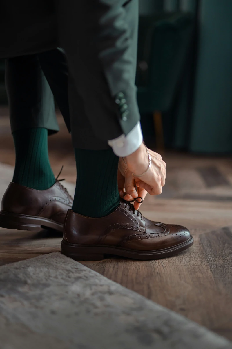 a man in a green suit trying on brogue shoes