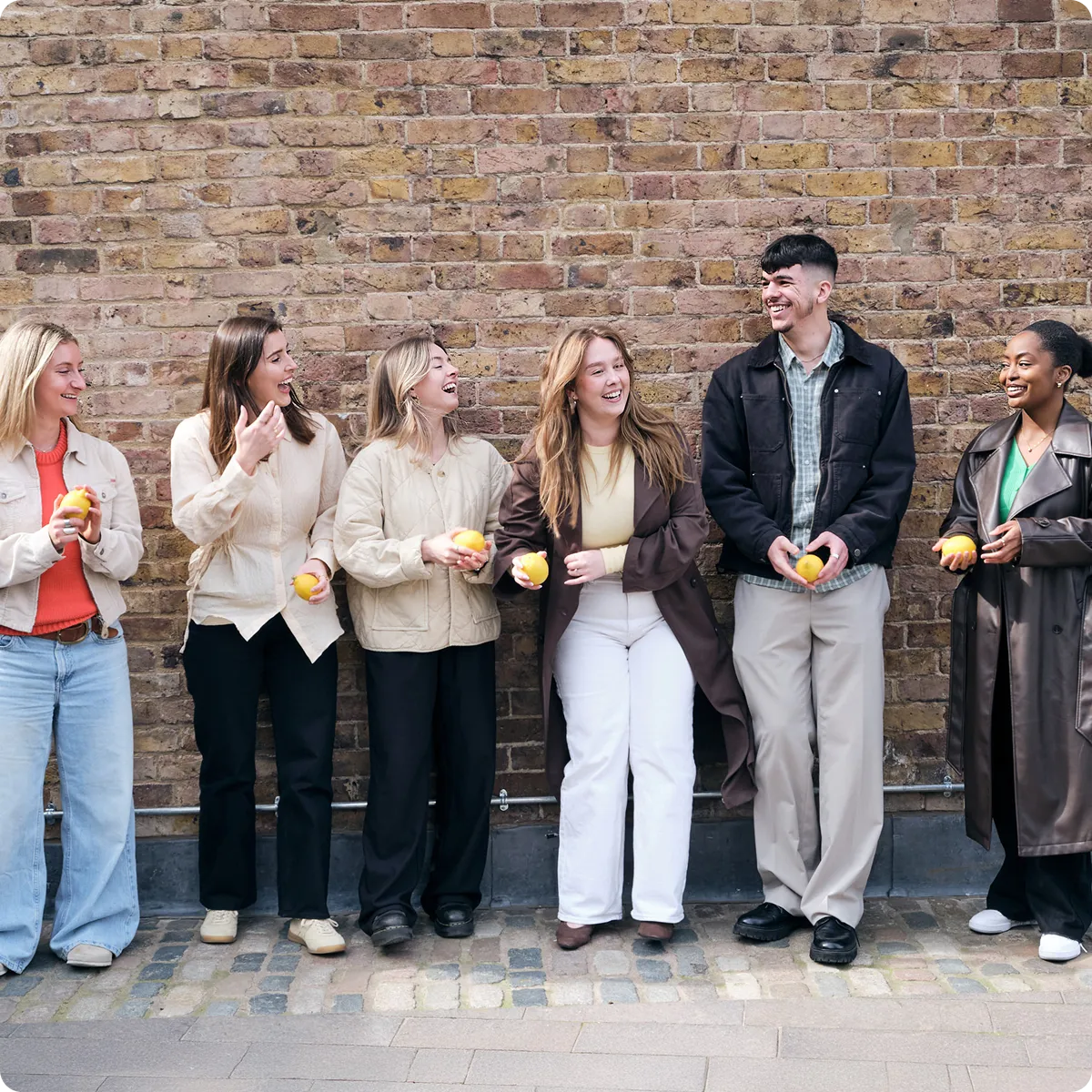 Lem Uhn Team standing against a brick wall, holding lemons and smiling at each other.