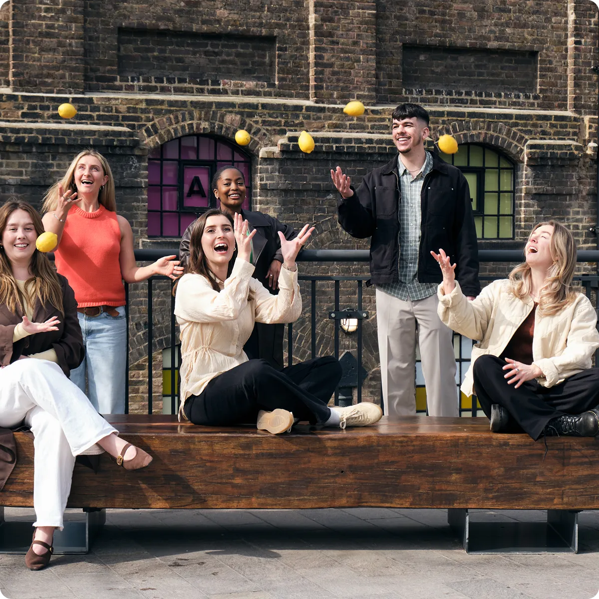 Lem Uhn Team smiling and tossing lemons in the air outdoors by a brick building.