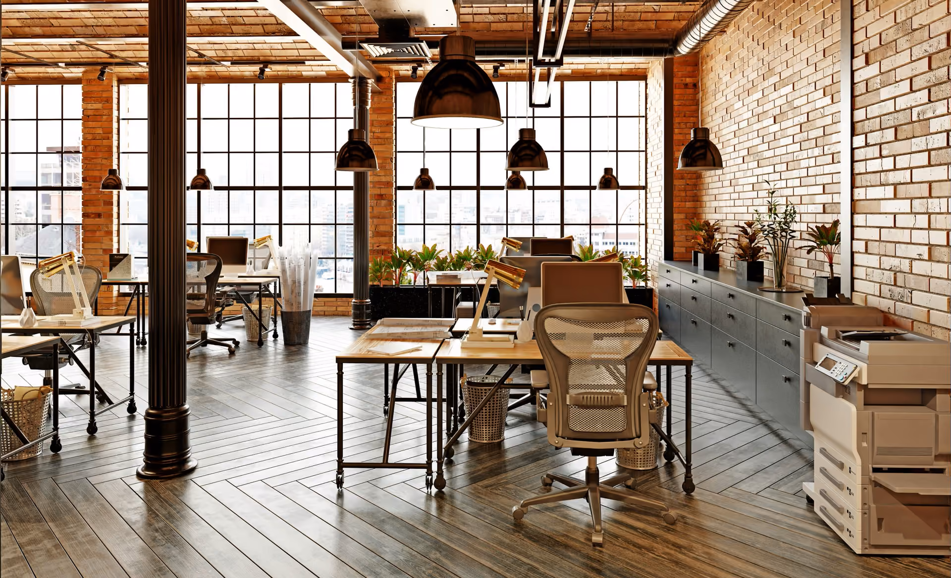 Modern open office with brick walls, large windows, plants, desks, chairs, and overhead lights.