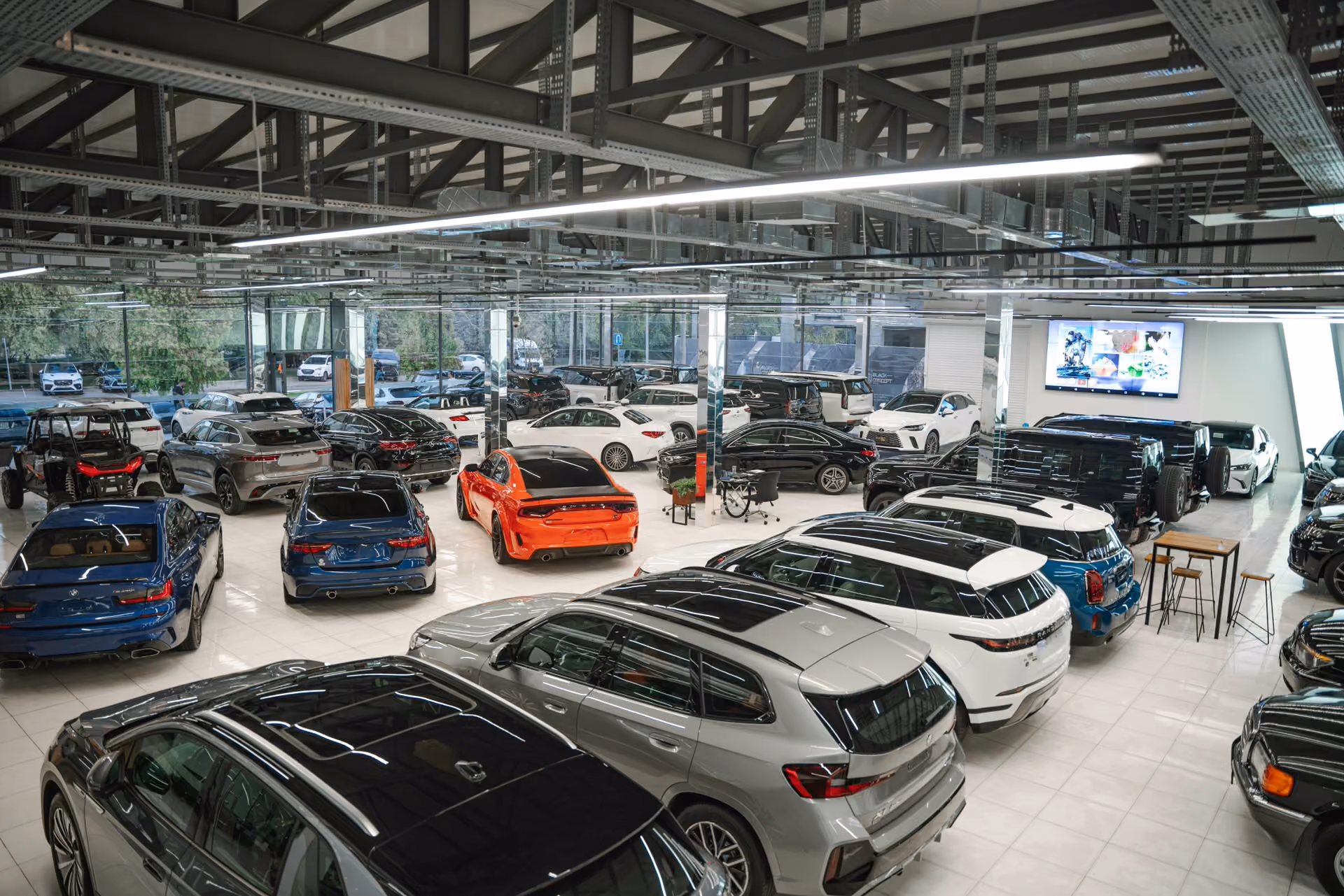 Modern car showroom with various SUVs, sedans, and a bright orange sports car under bright lighting.