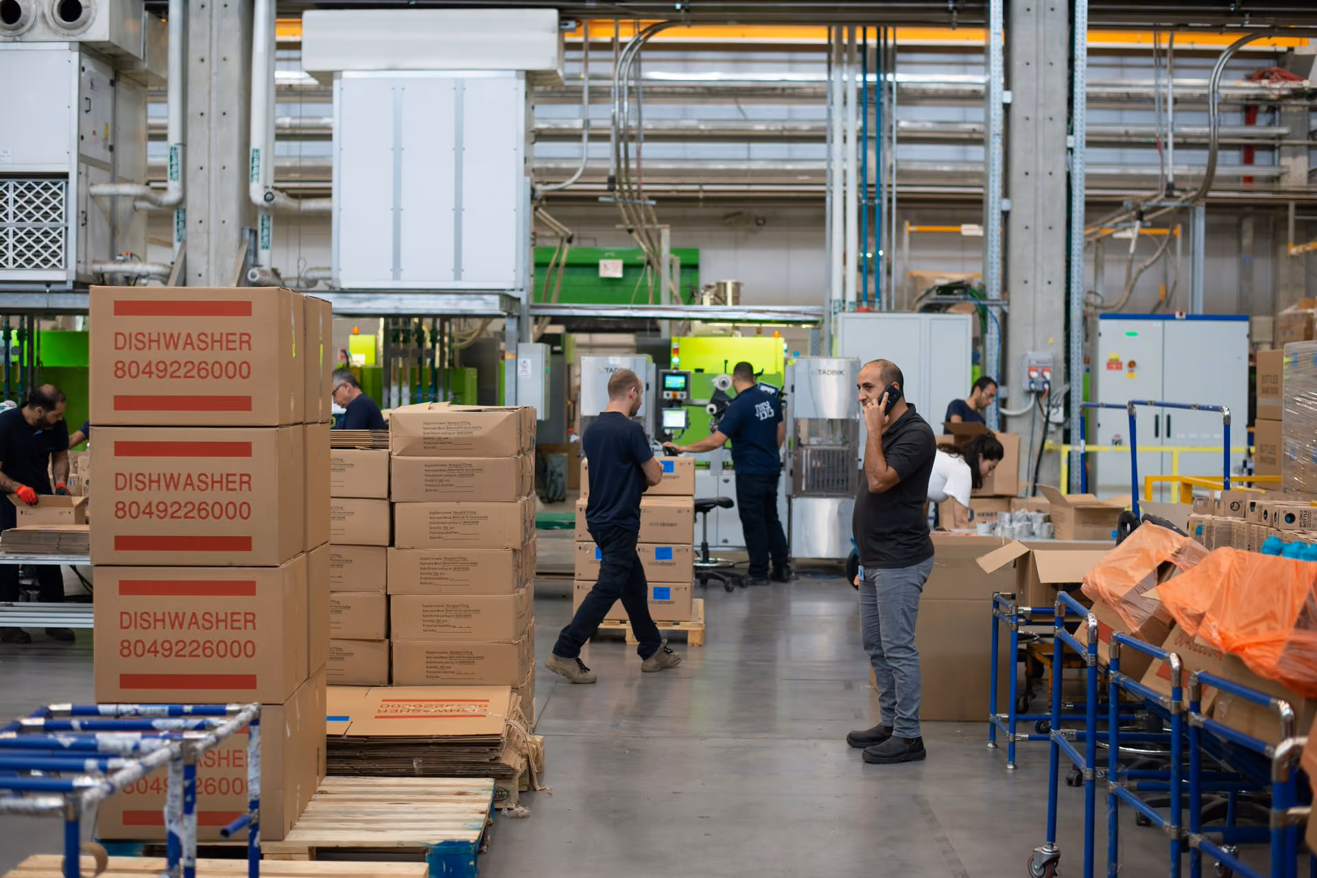 Warehouse with workers handling cardboard boxes labeled dishwasher amid industrial equipment.