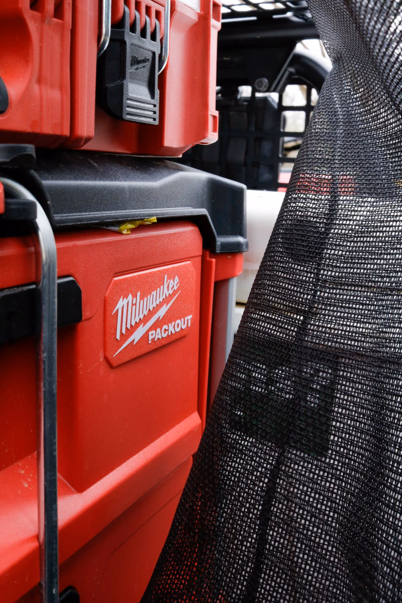 Close-up of a red Milwaukee Packout modular tool storage container with a black mesh fabric adjacent.