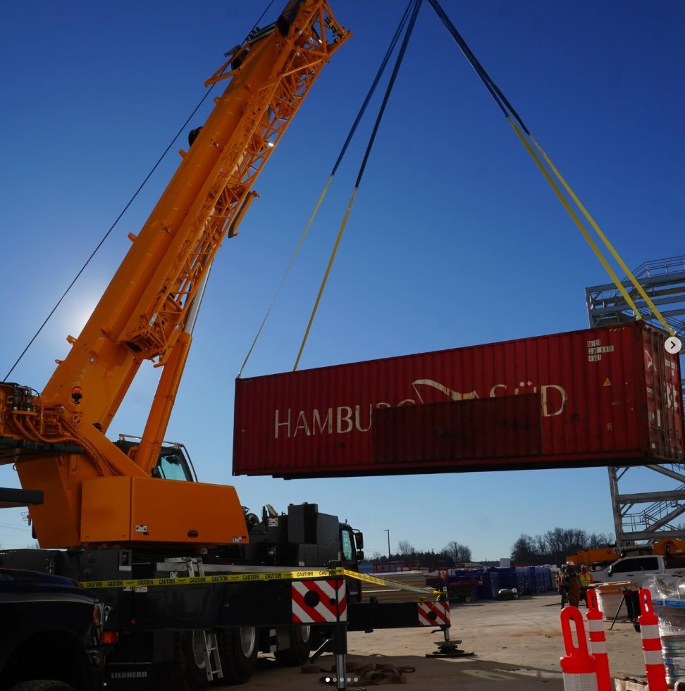 Orange Liebherr all-terrain crane lifting a Hamburg Sud shipping container at a port facility