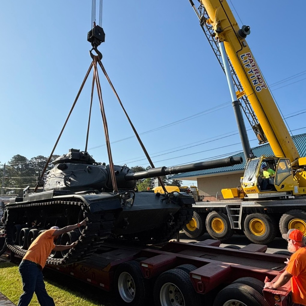 Patriot Lifting branded yellow Grove crane lifting an M48 Patton tank at a veterans memorial