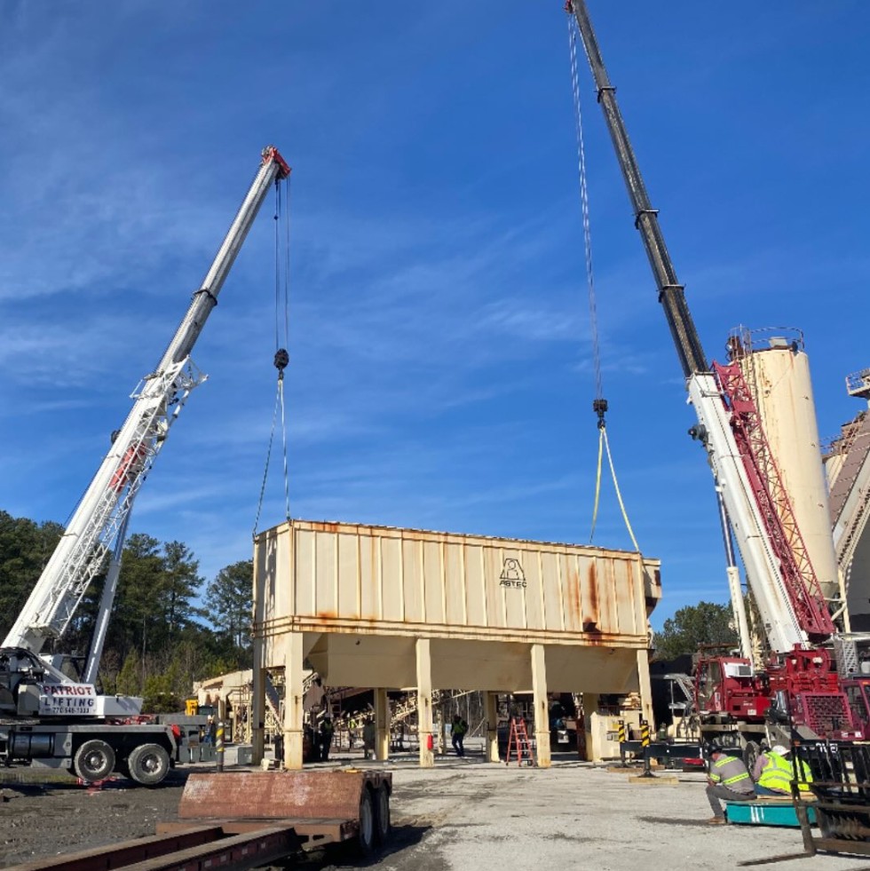 Two cranes performing a tandem lift of an Astec asphalt plant component, one branded Patriot Lifting