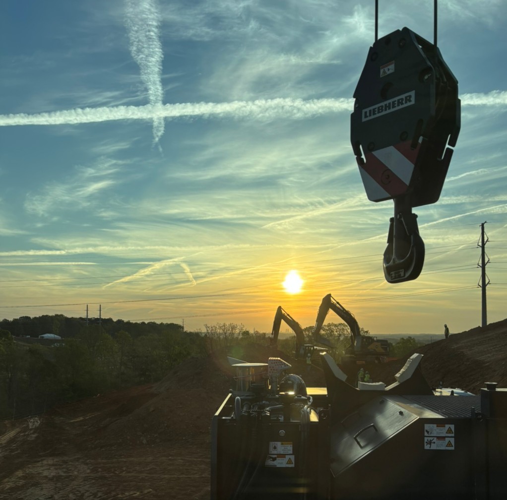 Liebherr crane hook block silhouetted against an orange sunset with excavators in an earthworks pit
