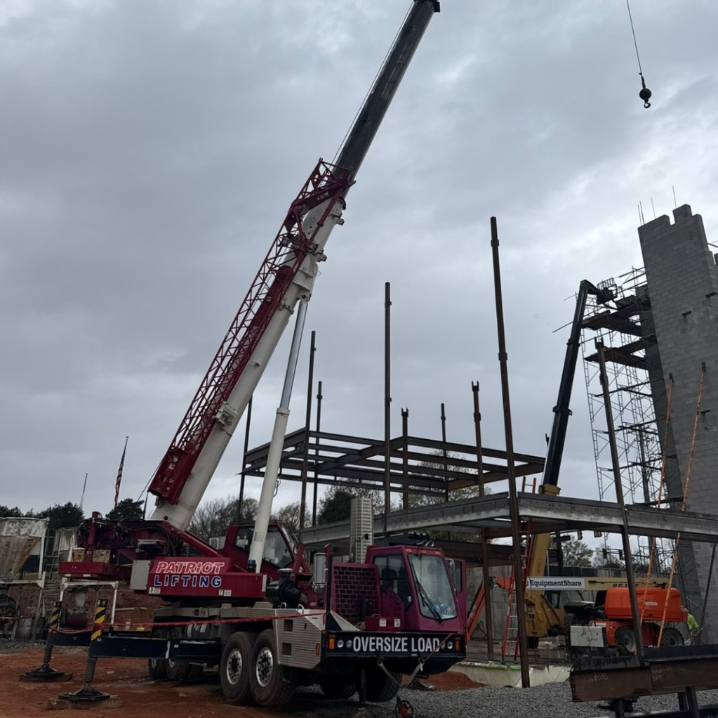 Patriot Lifting branded red crane with OVERSIZE LOAD signage at a steel erection job