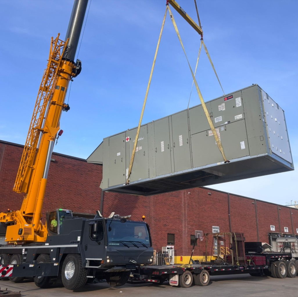 Yellow Liebherr crane lifting a large HVAC air handler onto a commercial rooftop