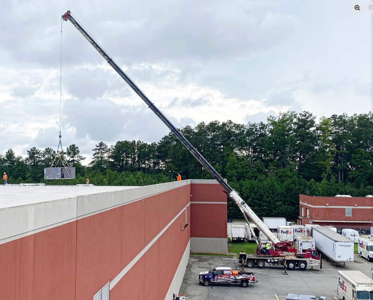 Patriot Lifting red crane lifting an HVAC unit onto a commercial warehouse rooftop