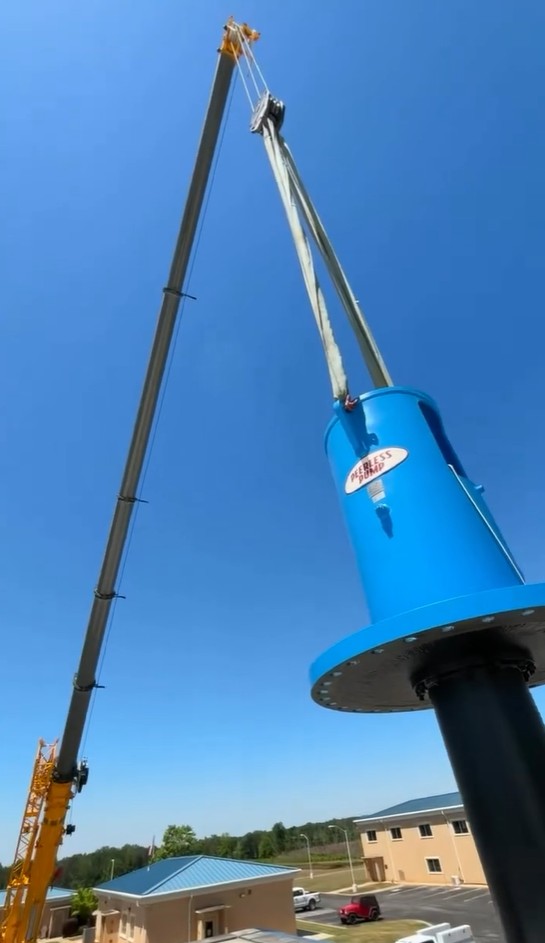 Crane lifting a blue Peerless industrial water pump into position at a utility facility
