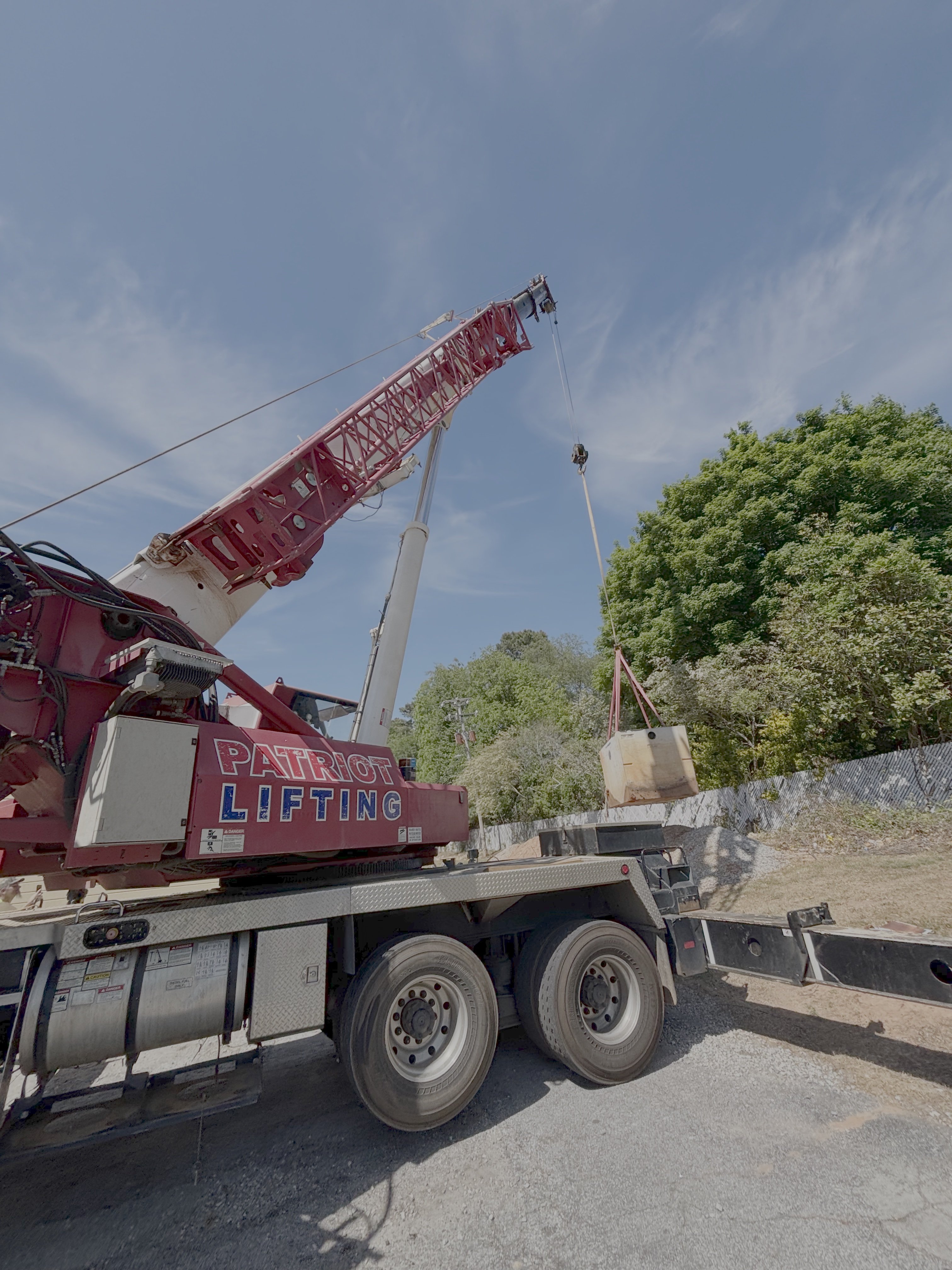 Patriot Lifting branded red and white Terex TMS9000E boom truck lifting a small cabin