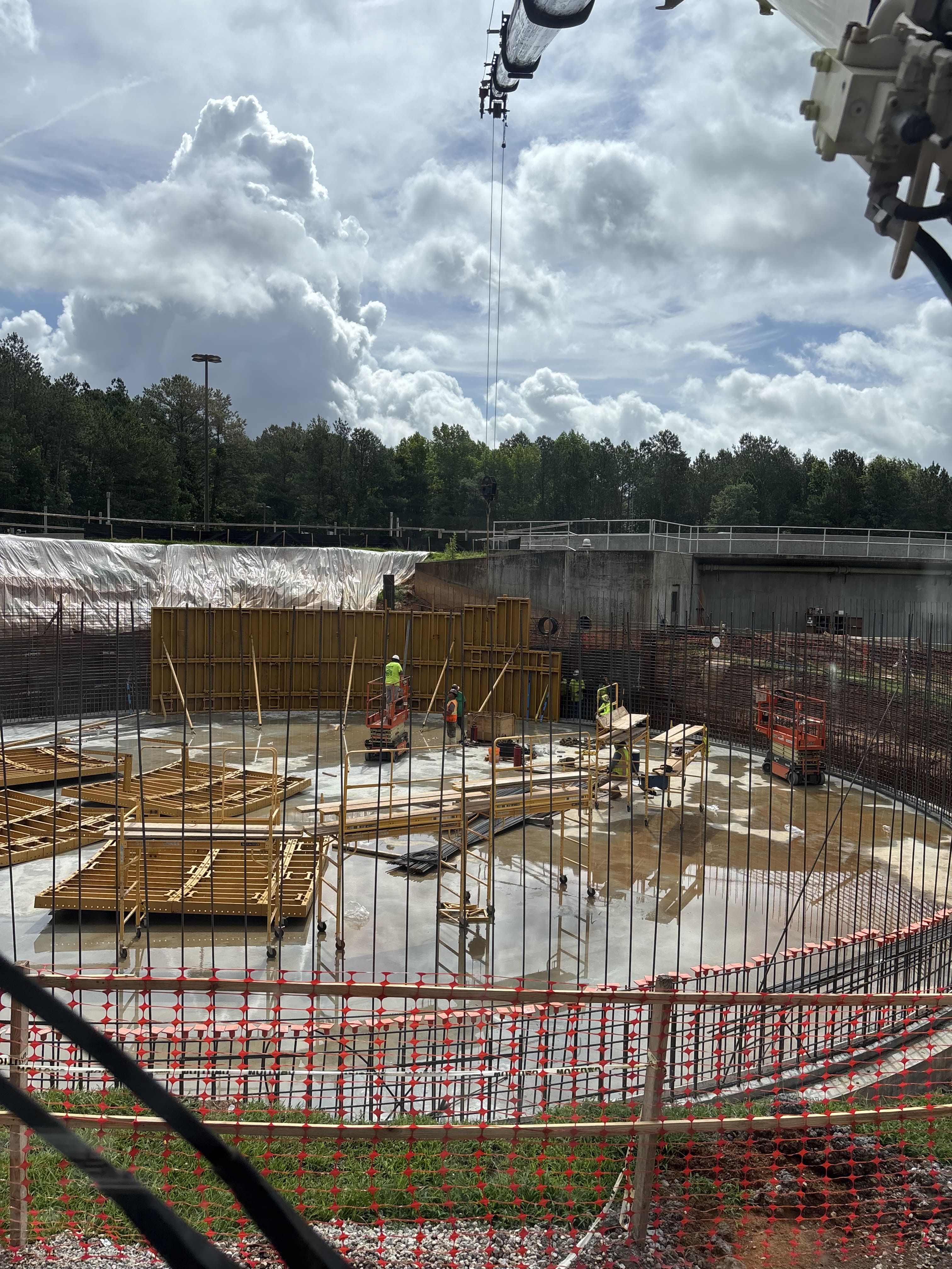 Patriot Lifting crane boom reaching over a circular concrete wastewater treatment tank under construction as crews set forms and rebar