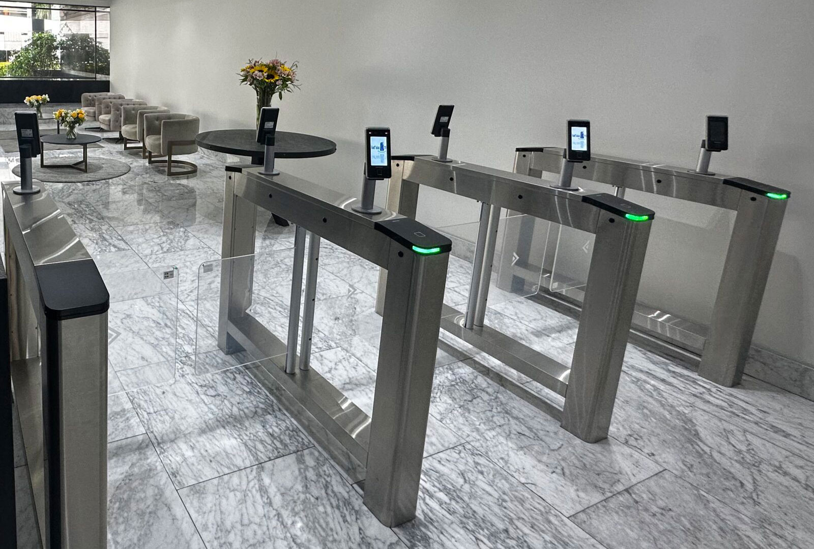 Modern security turnstiles with digital screens in a sleek lobby with marble flooring and seating area.