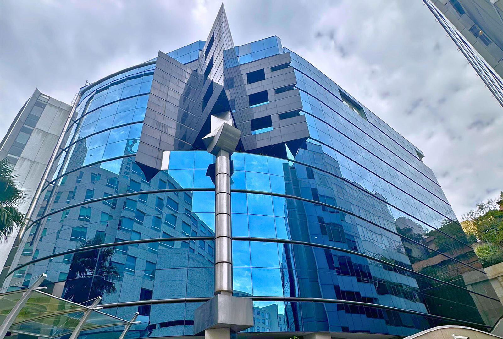 Modern glass building with reflective blue windows showing nearby buildings and sky.