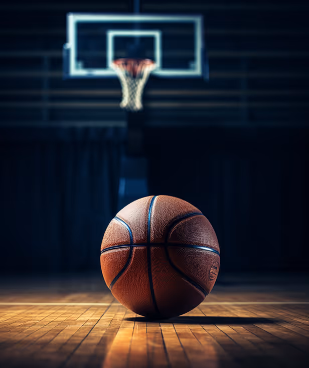 Basketball resting on a wooden court floor with a hoop and backboard blurred in background.