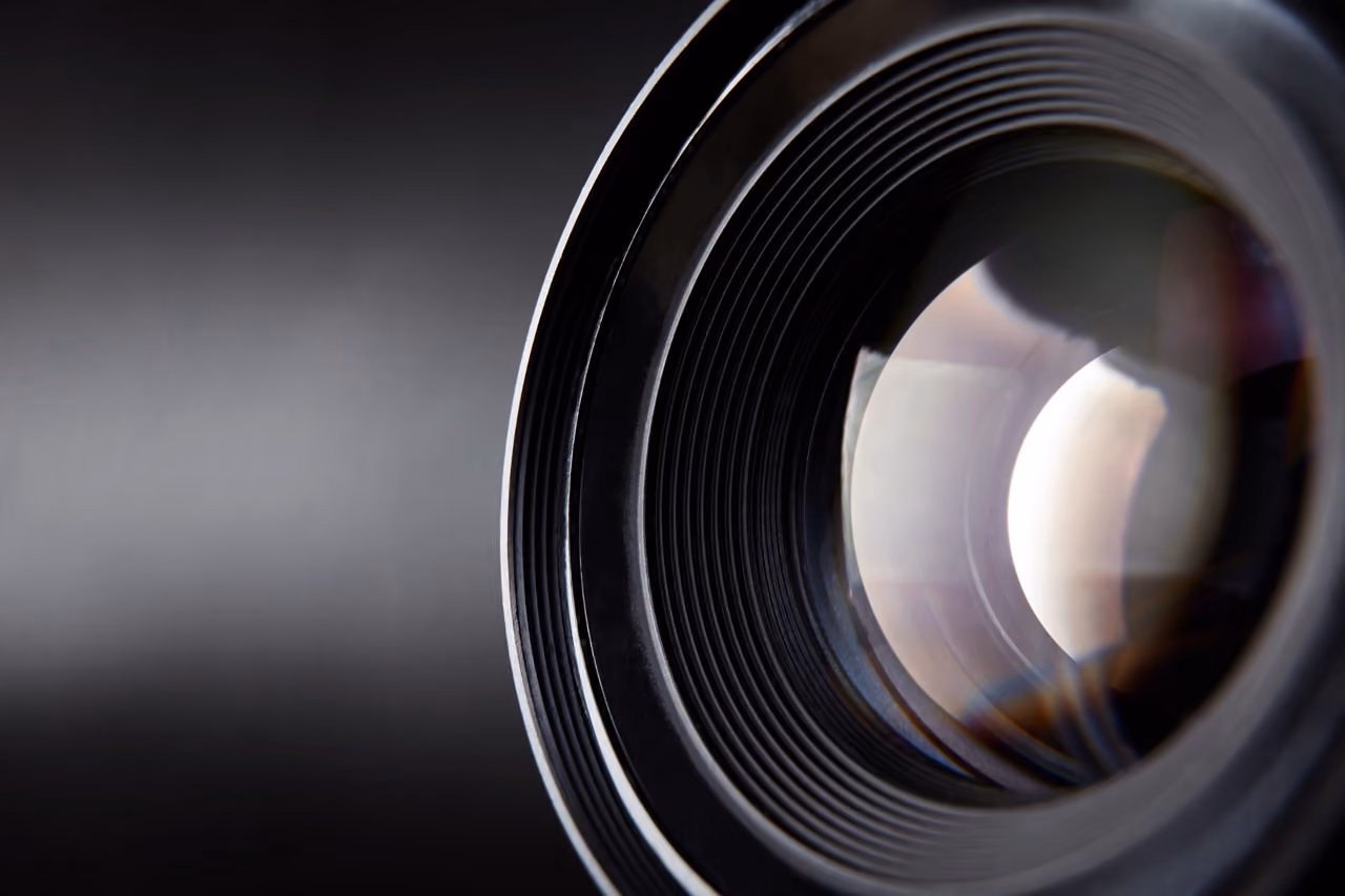 Close-up view of a camera lens with reflections and grooves against a dark background.