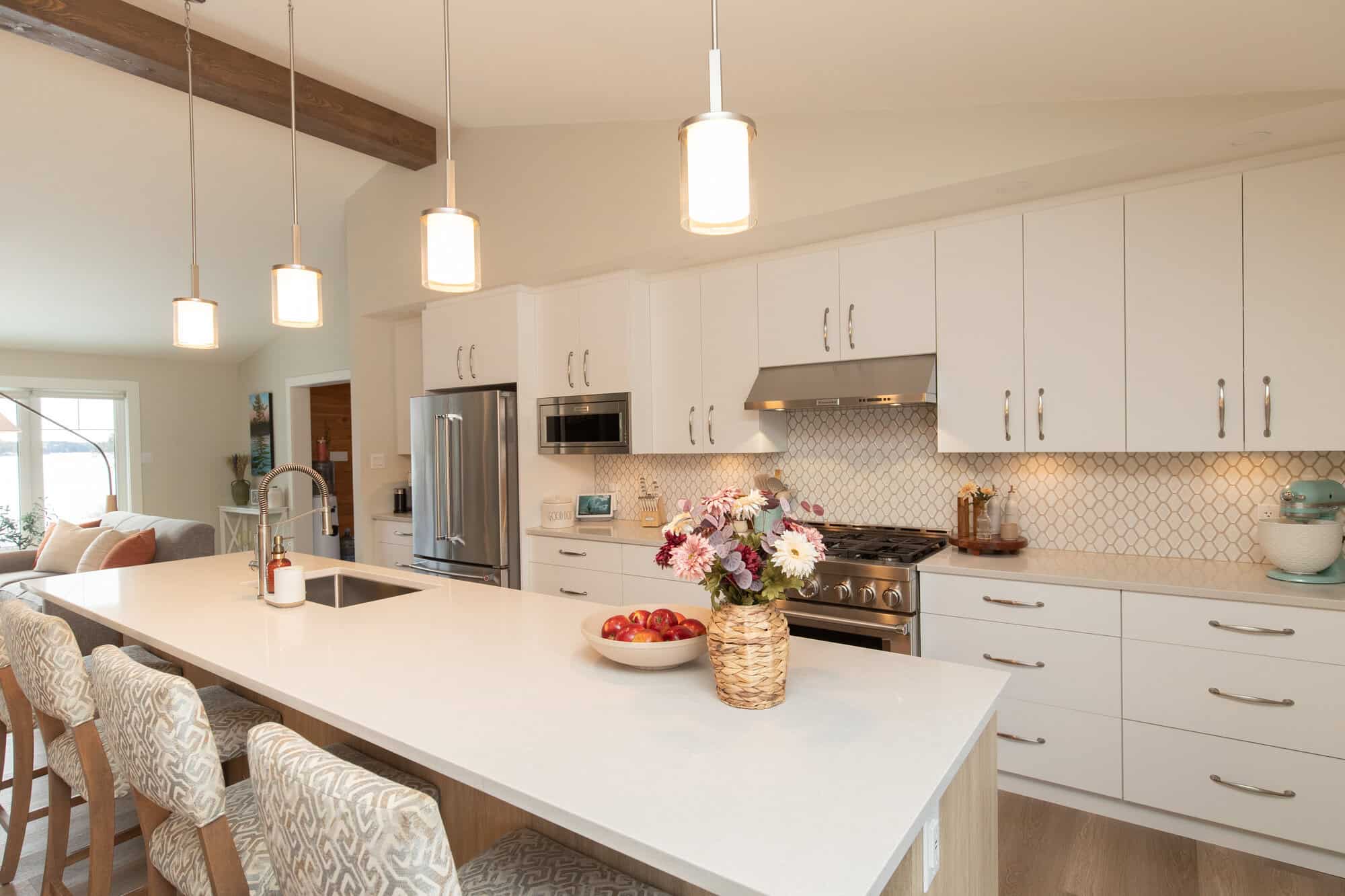 Modern kitchen with white cabinets, a large island, hanging lights, and stainless steel appliances.