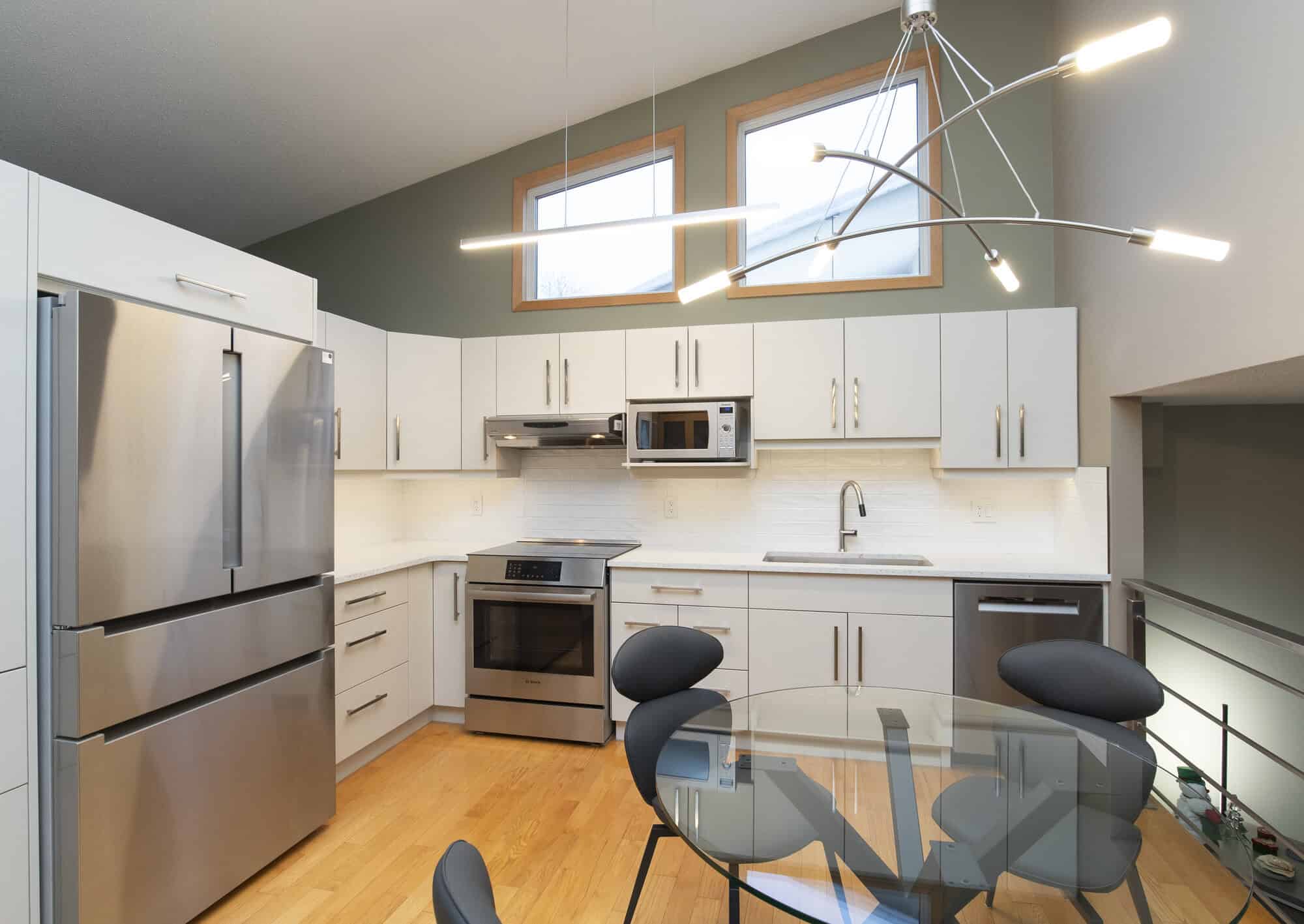 Modern kitchen with white cabinets, stainless steel appliances, and a glass dining table with black chairs.
