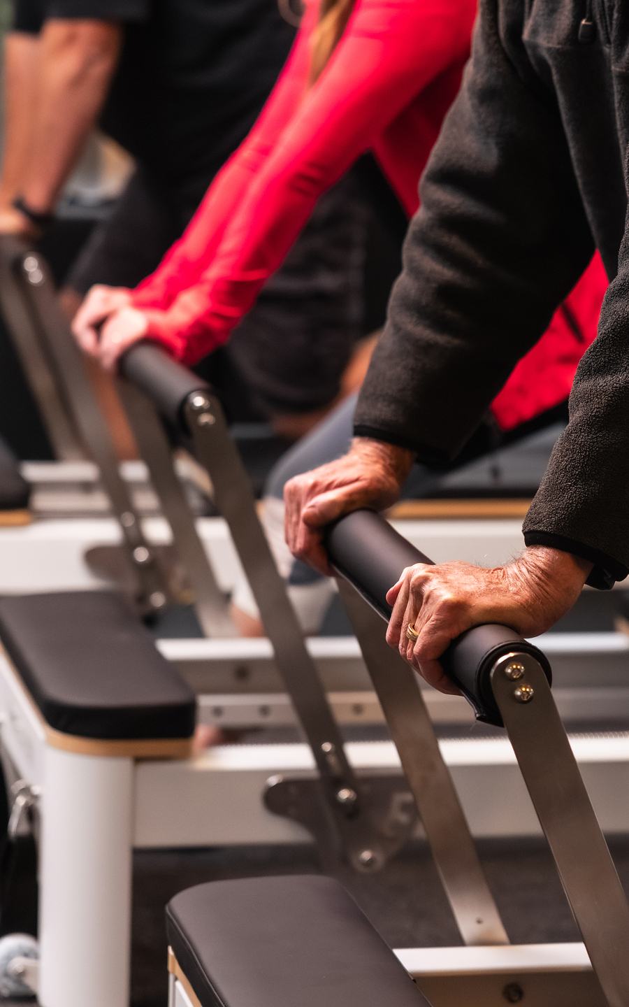 Close-up of hands gripping Pilates reformer bars during a group exercise session.