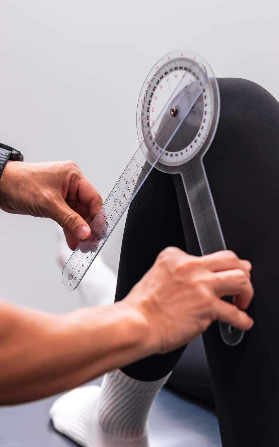 Physical therapist measuring knee bend angle with clear plastic goniometer on a patient.