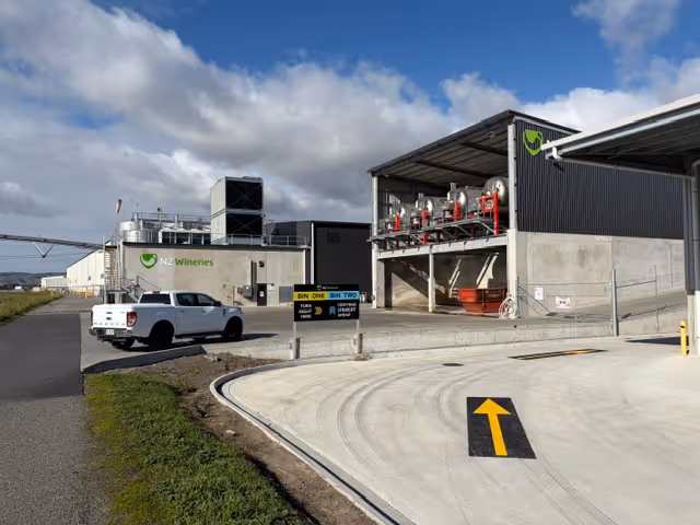 Industrial facility with NZ Wineries logo, white truck, and directional arrow on concrete road.
