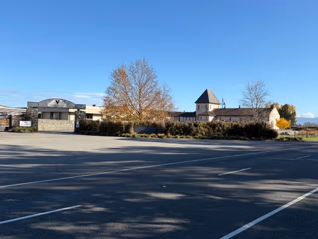 Empty parking lot in front of a building and trees with autumn leaves under clear blue sky.