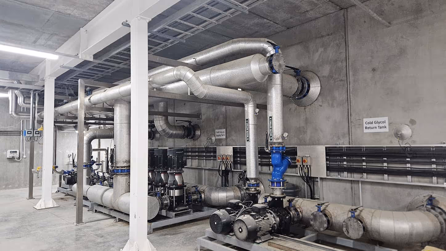Industrial pump system with large insulated pipes and control valves in a concrete utility room.