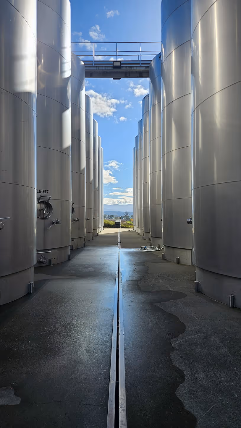 Tall stainless steel storage tanks aligned in two rows under a blue sky with scattered clouds.