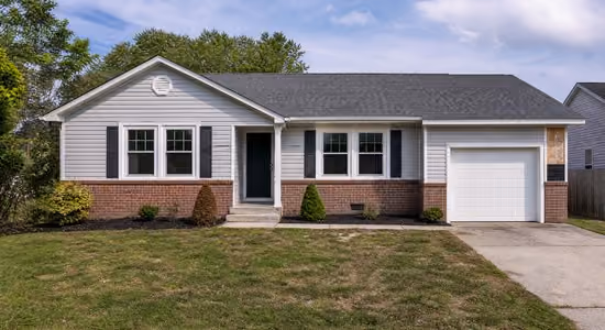 Single-story house with white siding, brick facade, black shutters, and attached garage under blue sky.