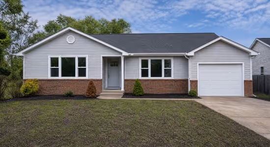 Single-story house with white siding, brick lower facade, front porch, and attached garage under blue sky.