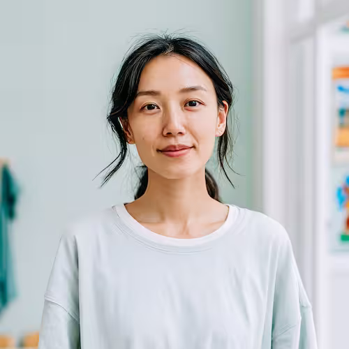 Smiling young Asian woman with dark hair wearing a white sweatshirt in a bright indoor setting.