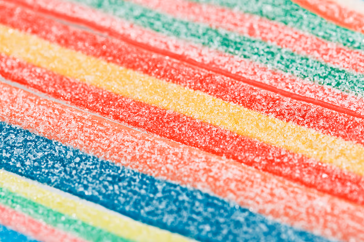 Close-up of colorful striped sour candy belts covered in sugar crystals.