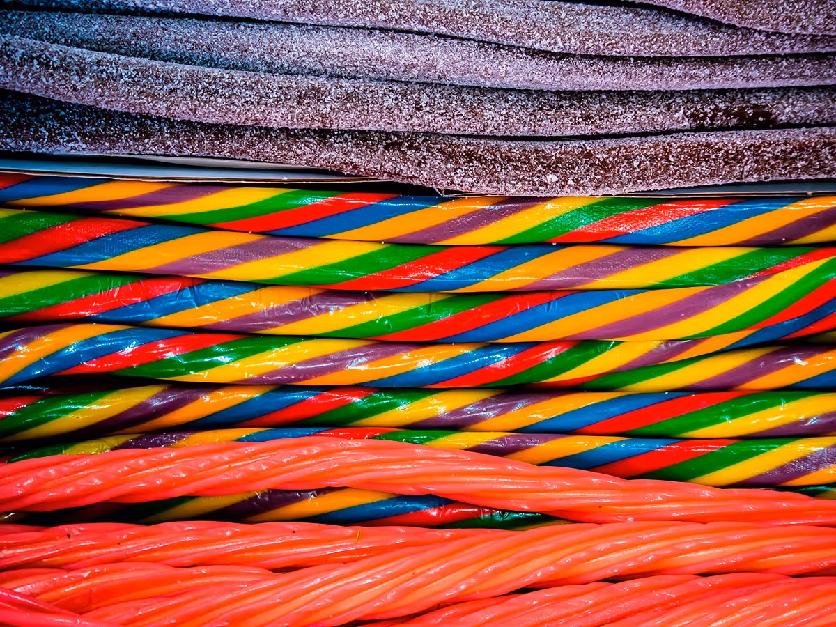 Close-up of colorful twisted candy ropes and flat sugar-coated candy strips stacked in rows.