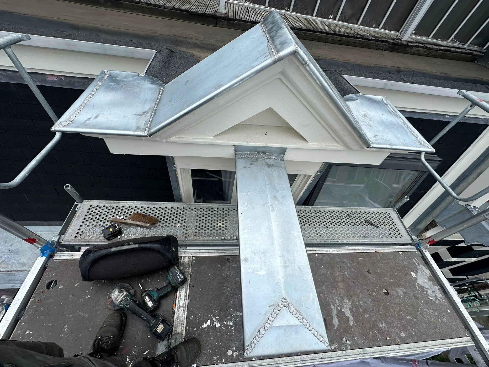 Dakgoteninstallatie op steiger met metalen dakbedekking en gereedschap zoals boren en een borstel.