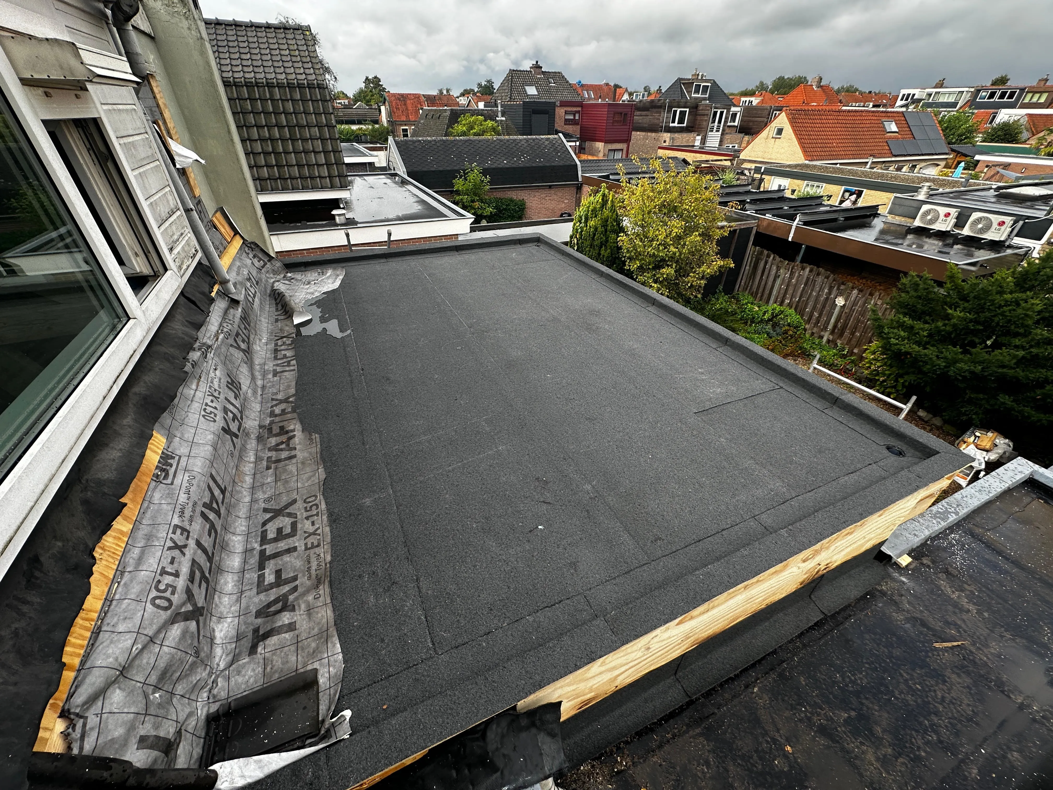 Plat dak in een woonwijk met dakrenovatie, deels bedekt met TAFITEX waterdichte folie.