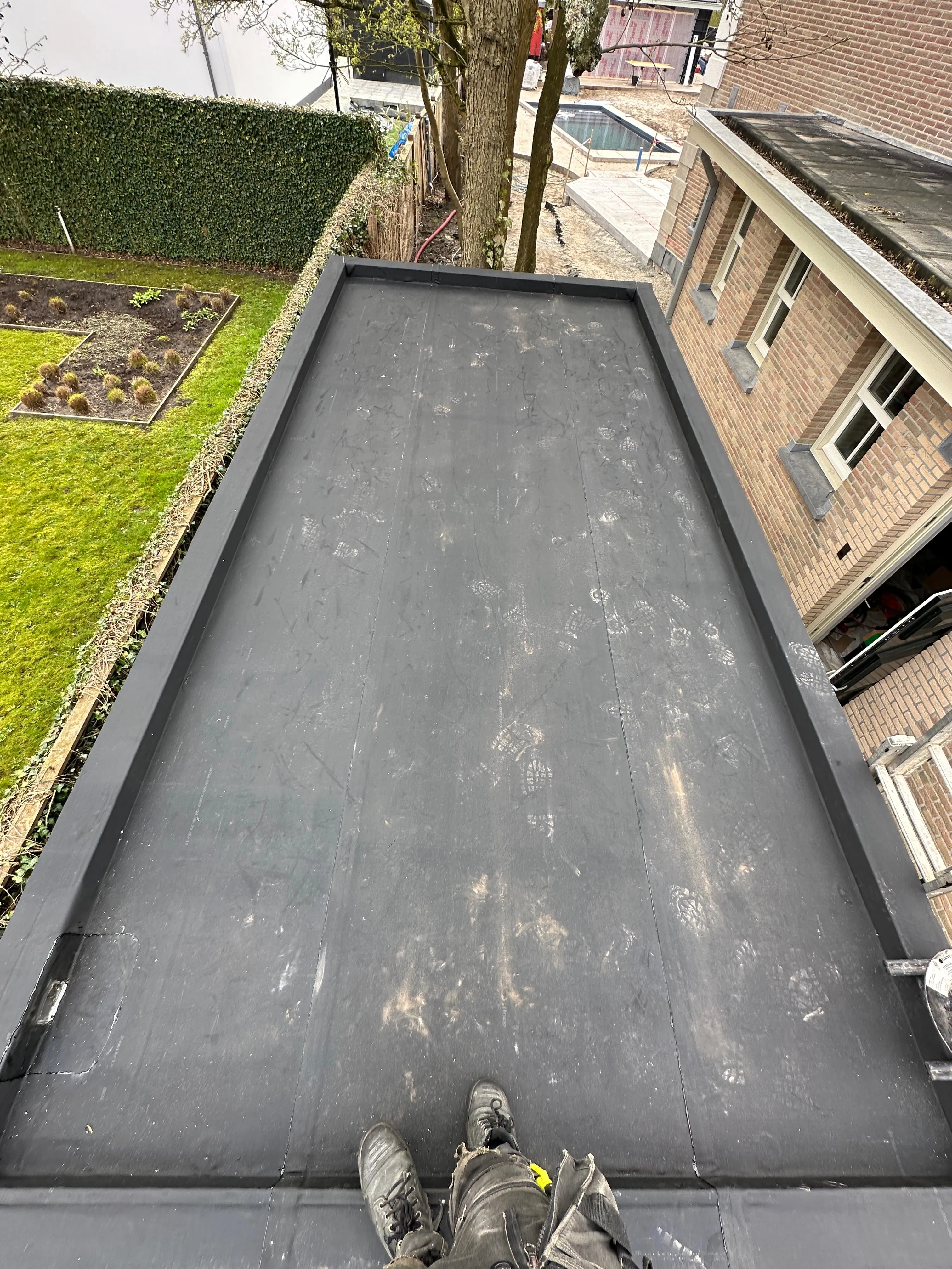 Zicht op een plat dak met schoenafdrukken en een paar laarzen op de voorgrond.