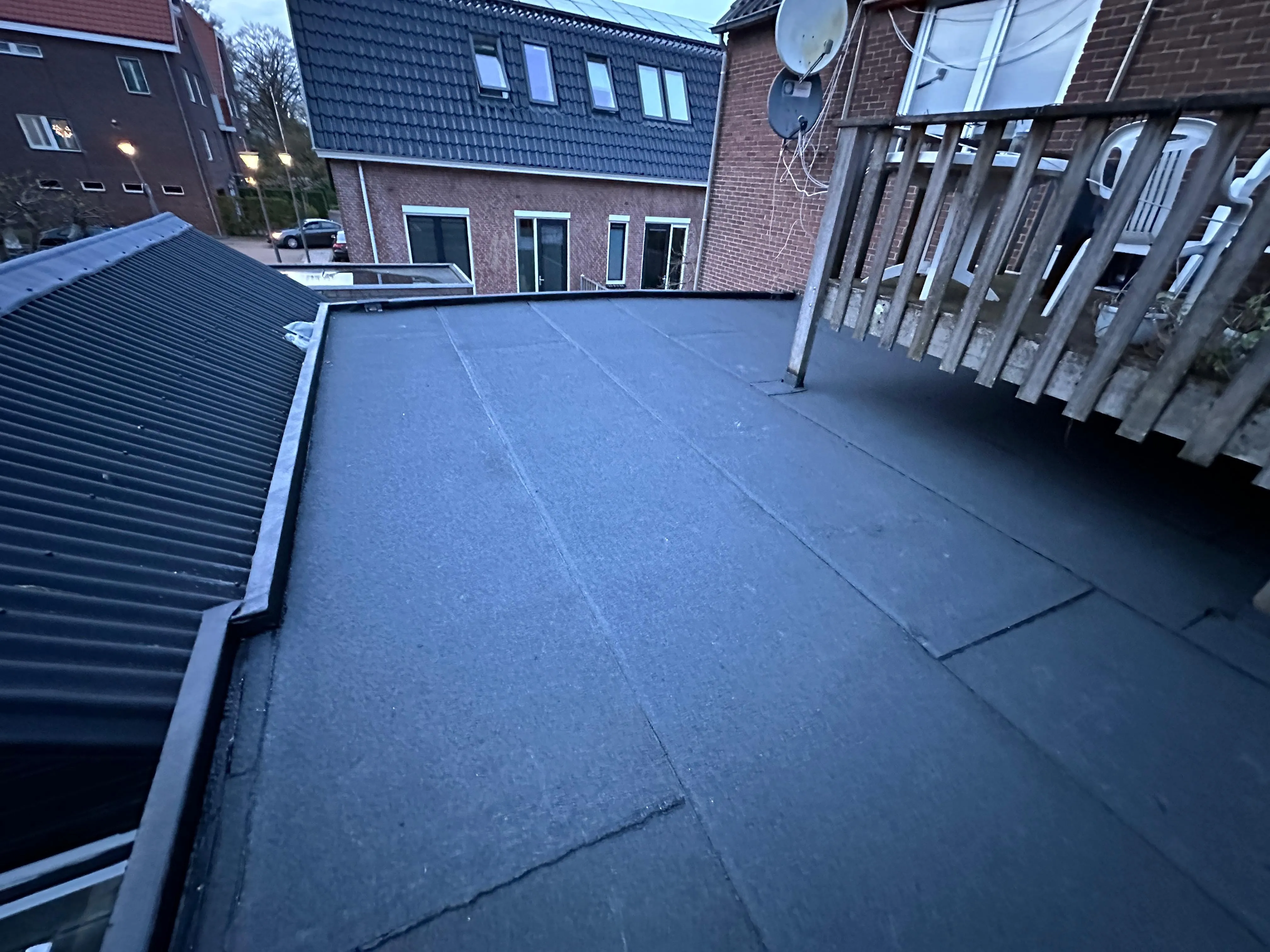 Plat dakterras met zwarte waterdichte bekleding en houten hekwerk aan een bakstenen huis.