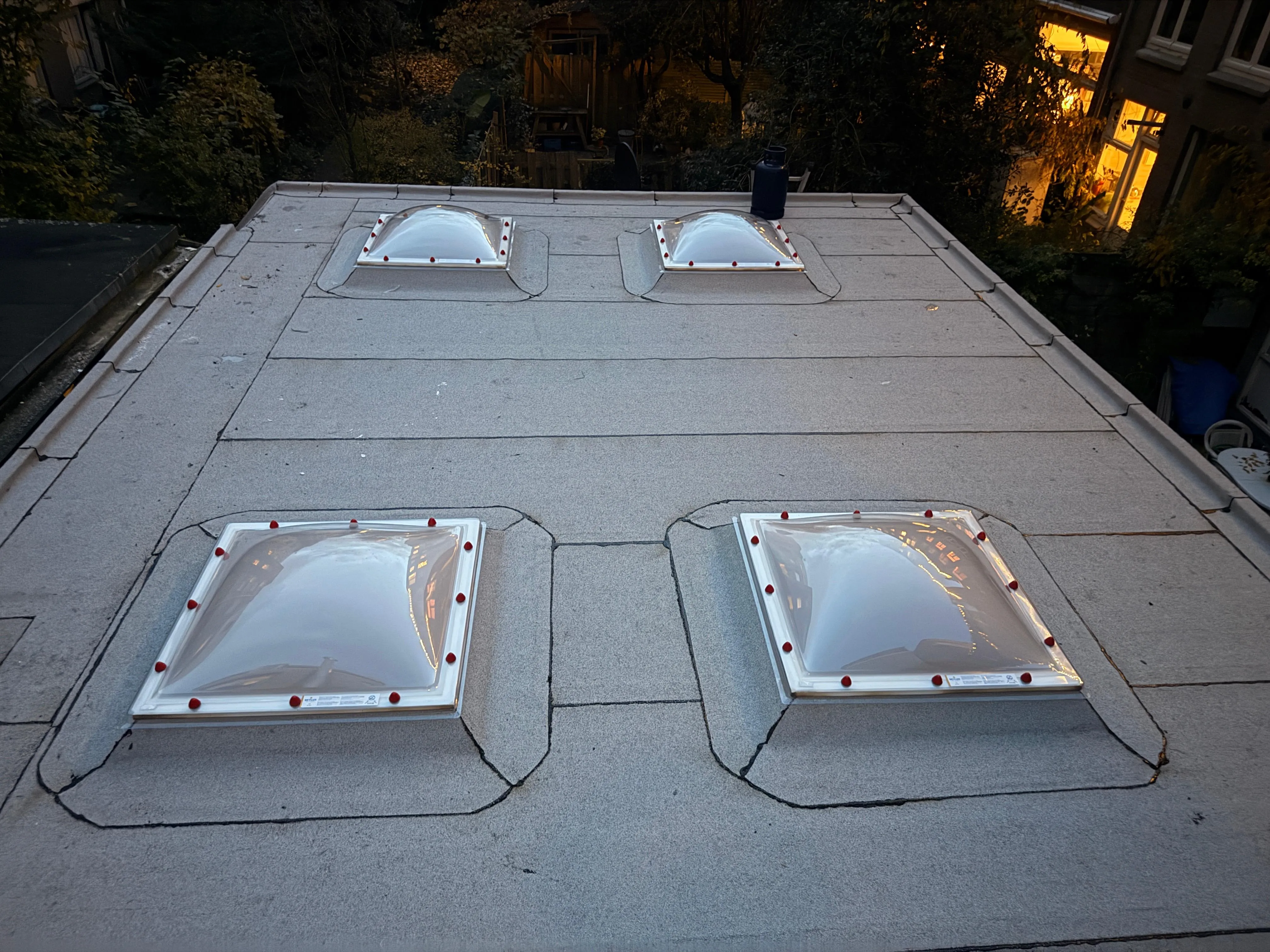 Plat dak met vier koepelramen aan de bovenkant van een gebouw bij avondlicht.