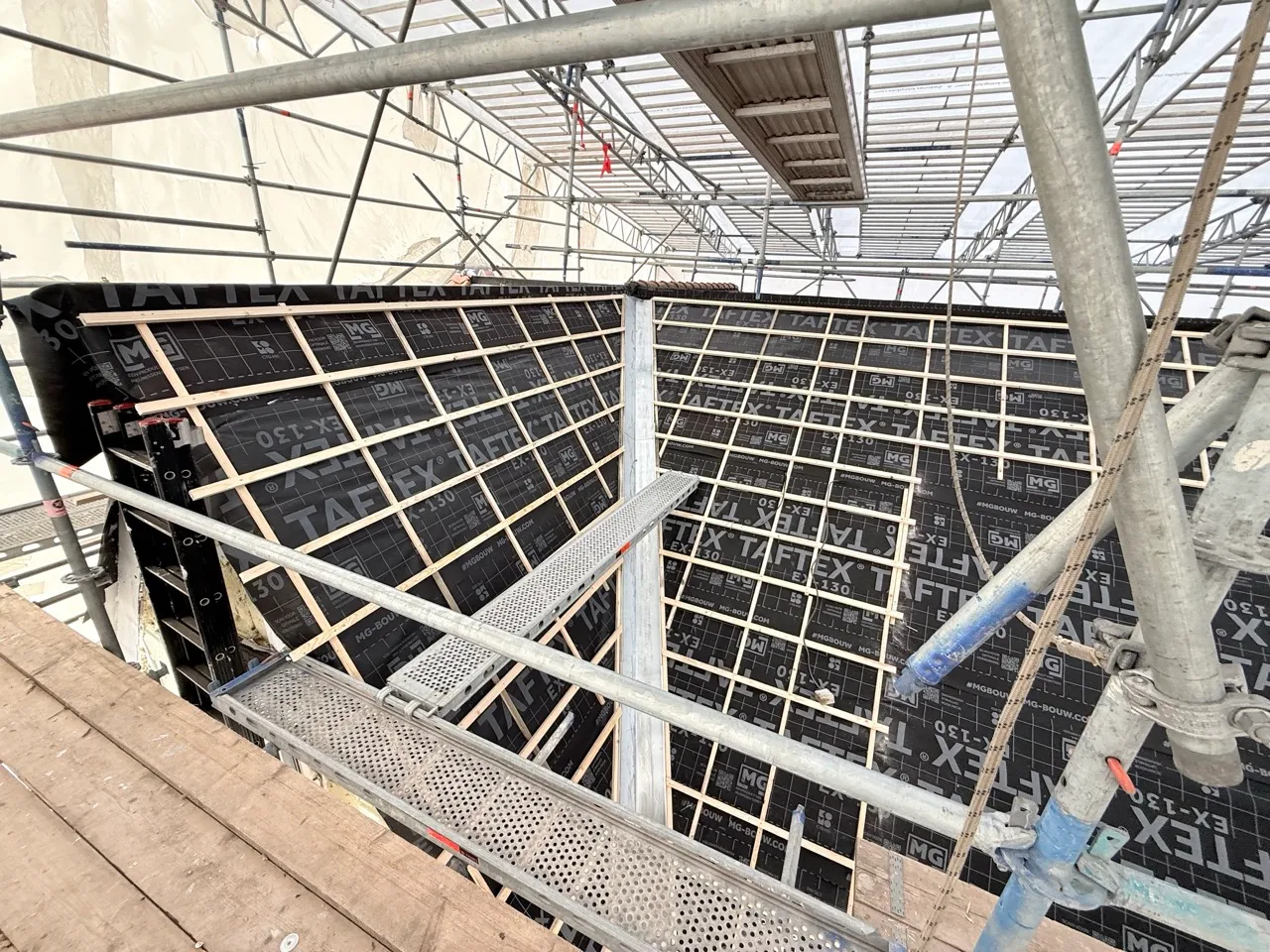 Steiger rondom een bouwproject met zwarte Taftex-dampremmende folie en houten latten.