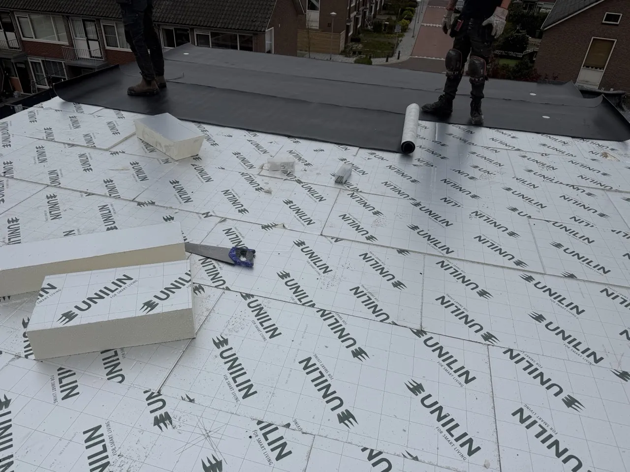 Roofing project with white UNILIN underlayment panels and two workers installing black roofing material.