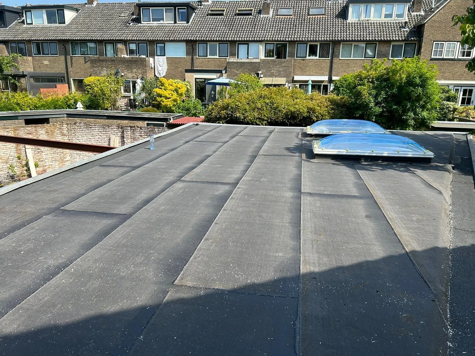 Flat roof with two skylights, a water bottle, and residential buildings and greenery in the background.