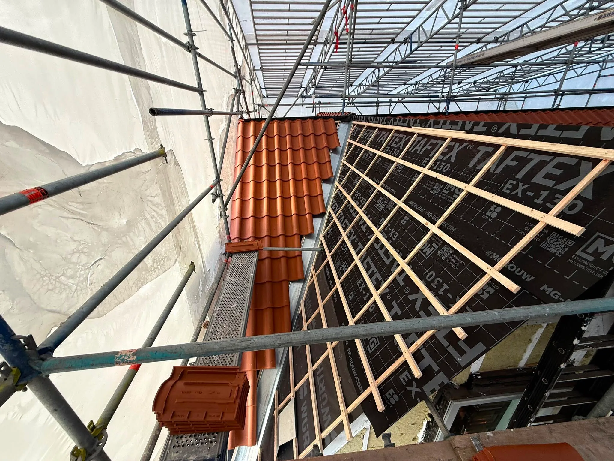 Construction scaffolding around a roof mid-installation with orange tiles and wooden supports.
