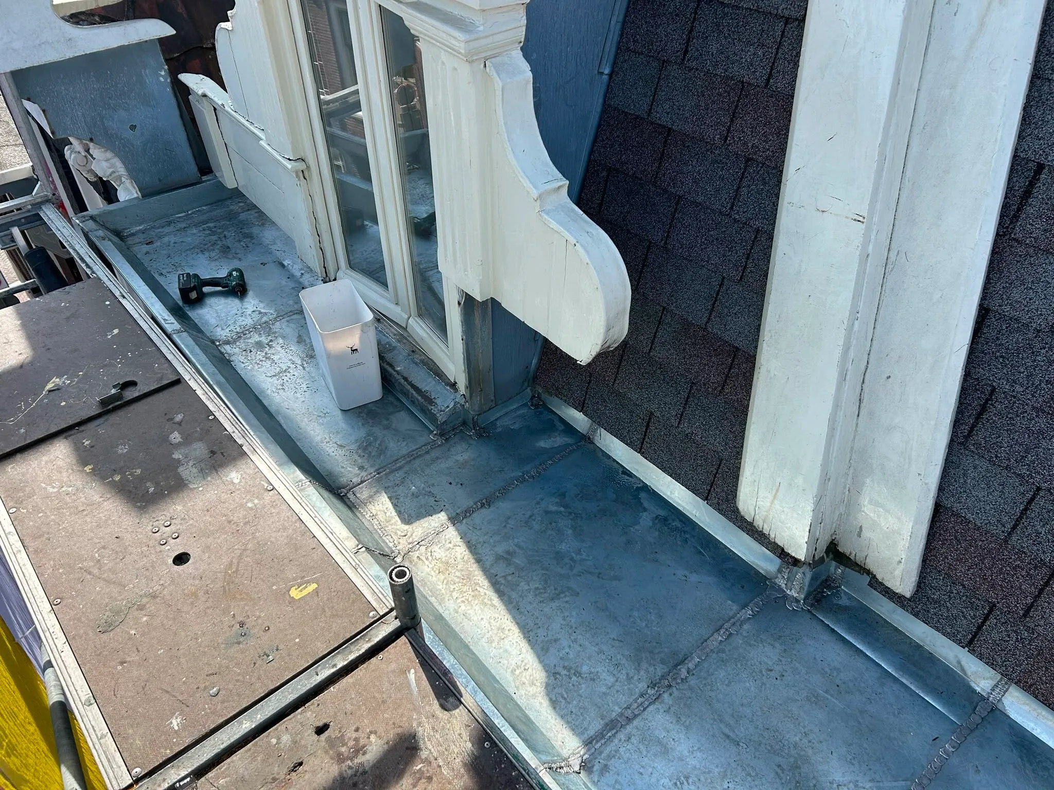 Roof edge with metal flashing, white wooden trim, a small container, and a cordless drill on the surface.
