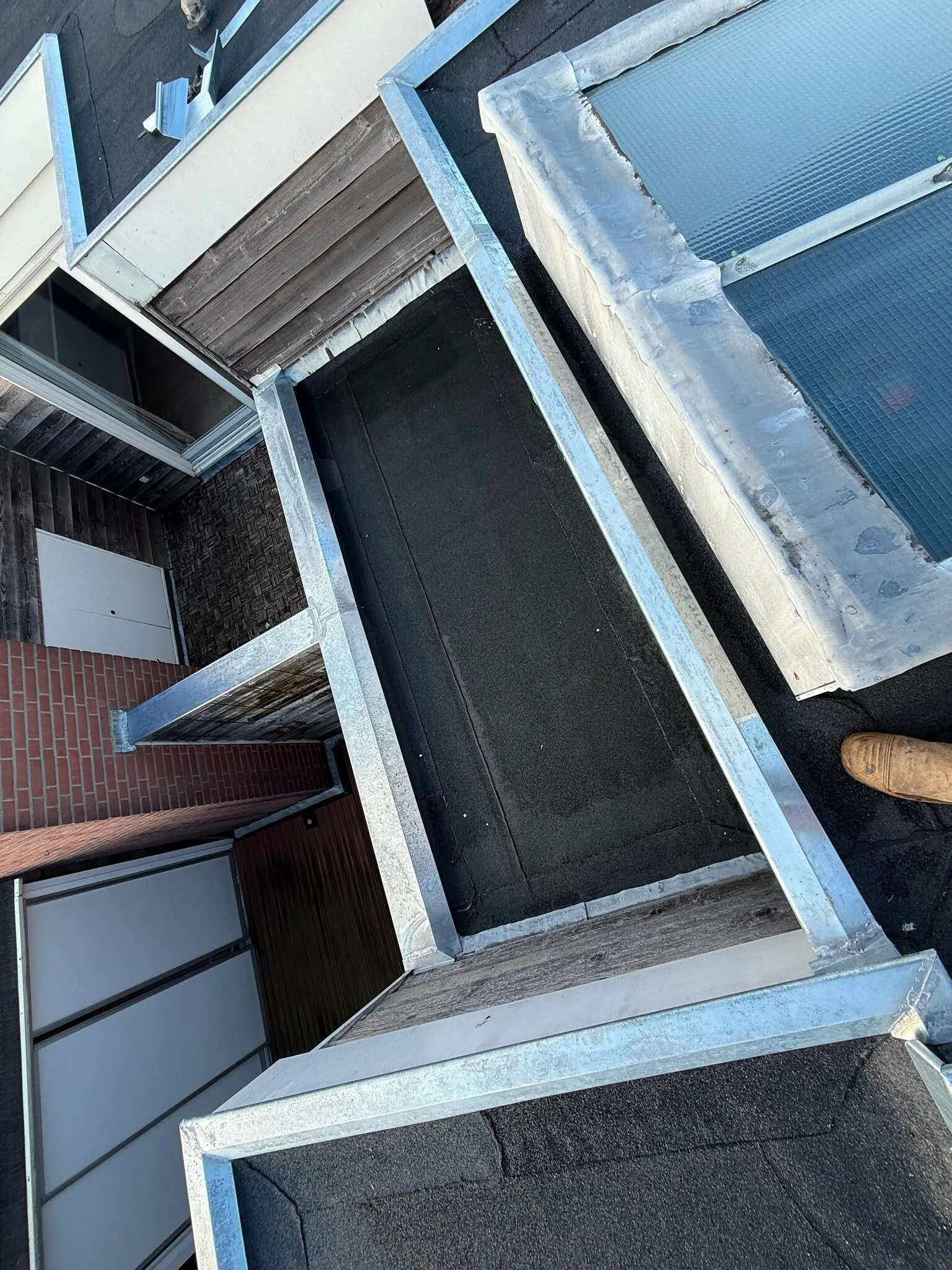 Roof area with metal-framed skylights, wooden siding, and brick exterior near a small door and window.