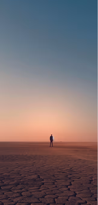 A lone person standing on cracked dry ground under a vast sunset sky.