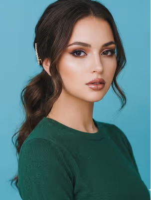 Young woman with long dark hair in ponytail wearing a green sweater and neutral makeup against turquoise background.