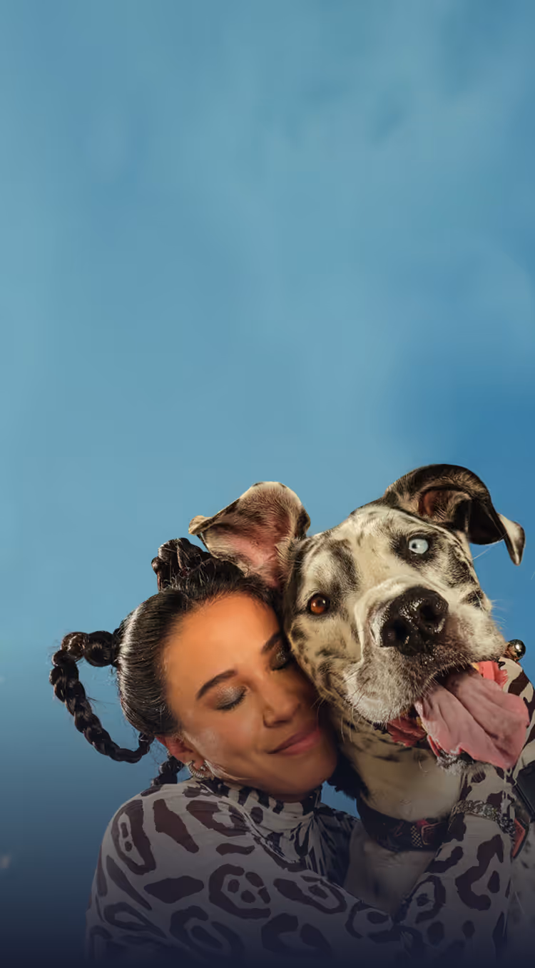 Woman with braided hair hugs a large dog with heterochromia against a blue background.